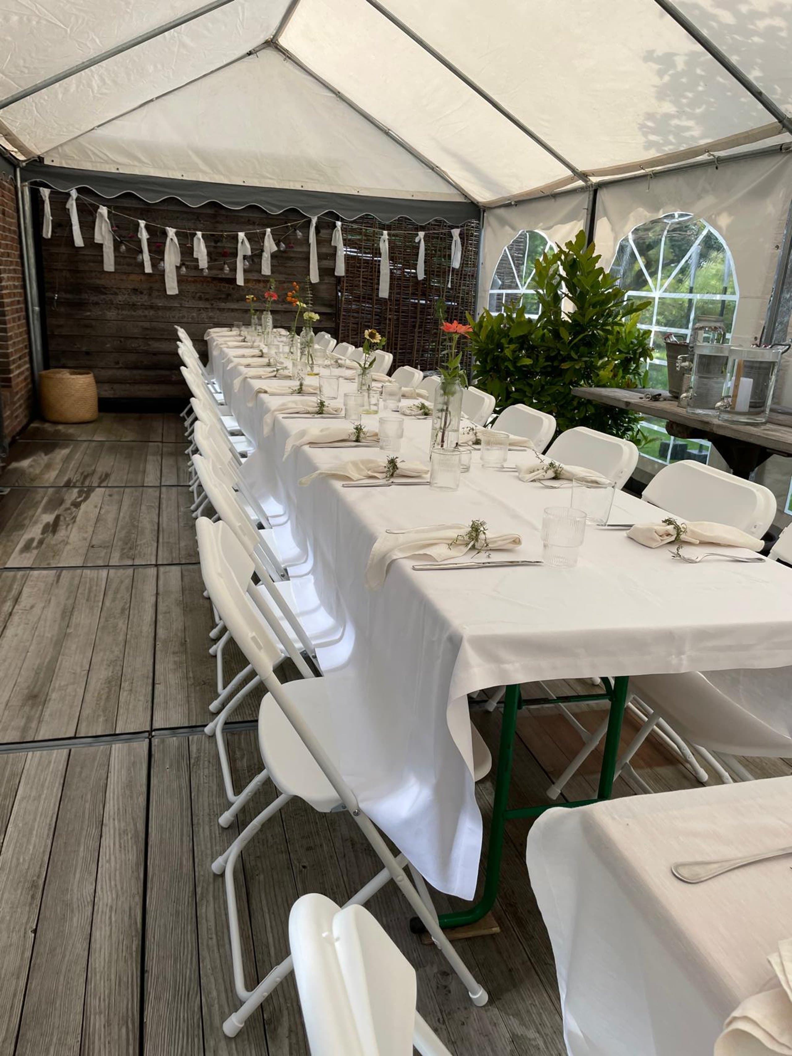 Lange Festtafel mit weißen Stühlen unter einem Zelt