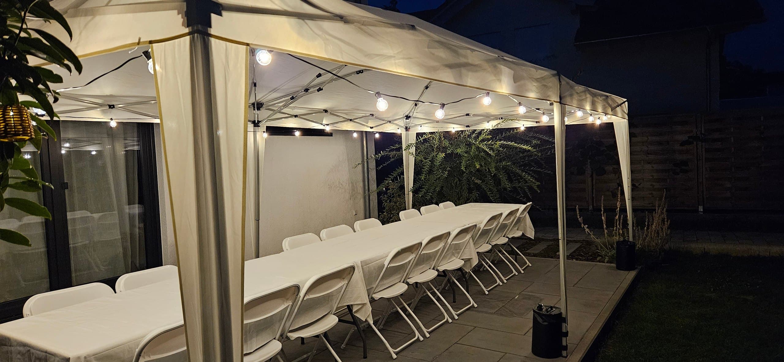 Weißes Partyzelt bei Nacht mit langer gedeckter Tafel und Lichterketten